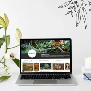 A laptop displaying the online collection of Liebig and Eucalol cards on the screen. Flowers, a book, and a candle are arranged on the table around it.