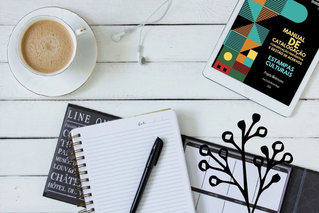 Xícara de café, caderno, caneta e tablet com a capa do Manual de Estampas Culturais.